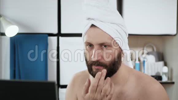 人在眼睛周围涂上奶油穿着毛巾在浴室里的一个很有魅力的男人把奶油涂在脸上视频的预览图