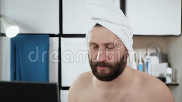 男人在做面部按摩一个穿着毛巾在浴室里长着迷人胡须的男人正在做手按摩视频的预览图