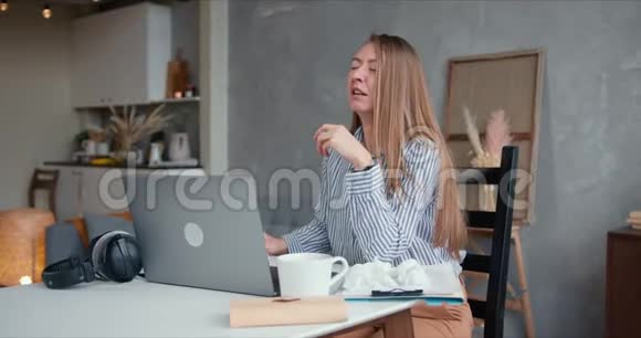 生病的年轻漂亮的高加索女人咳嗽和打喷嚏用纸巾用笔记本电脑在家工作隔离视频的预览图