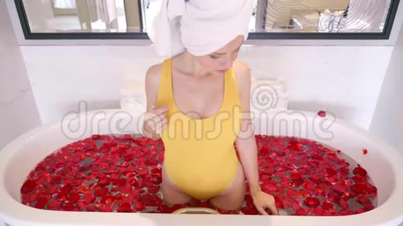 美丽的性感女孩穿着黄色泳装在浴室里放松与红色玫瑰花瓣视频的预览图