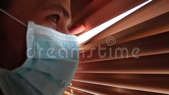 一个年轻的帅哥戴着医用口罩透过百叶窗看着视频的预览图