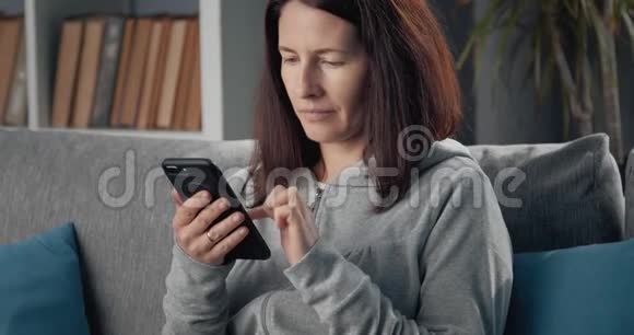 成熟的女士在家里使用智能手机视频的预览图