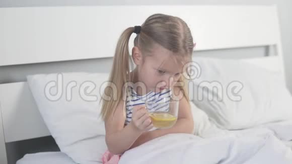 可爱的小女孩在家里的床上喝着柠檬茶视频的预览图
