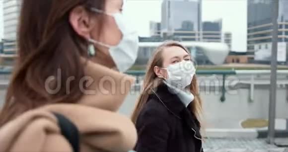 流行病保护两个年轻快乐的白人商业女性在隔离期间戴着口罩在城市街道上行走视频的预览图