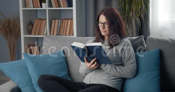 戴眼镜的快乐女士在沙发上看书视频的预览图