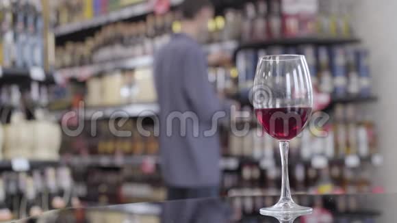 一杯昂贵的红酒在酒精超市的桌子上作为一个模糊的白种人用来脱酒视频的预览图