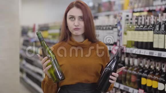 有魅力的红发白种人女人在酒精超市里选择红葡萄酒和白葡萄酒欢快的肖像视频的预览图