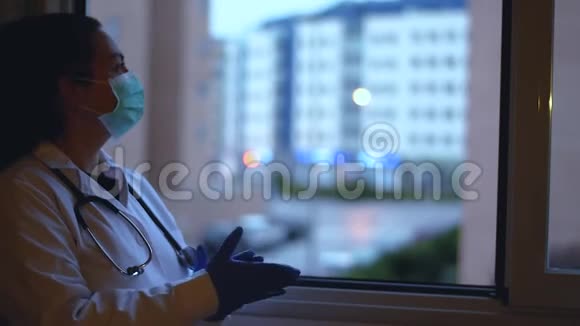 带着面具和听诊器的女医生在窗外拍手视频的预览图