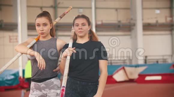 撑杆跳训练两名年轻女子站在体育场上举着杆子看着镜头视频的预览图