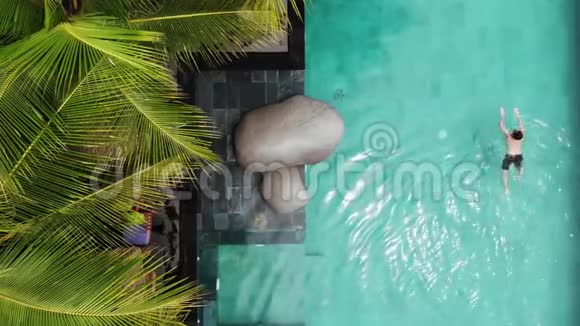 无人机鸟瞰男子游泳在豪华游泳池与蔚蓝的水和棕榈树和丛林在乌布德巴厘岛假期视频的预览图