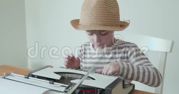 戴帽子的小男孩正在学习用一台旧的便携式打字机打字视频的预览图
