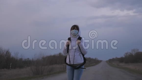 免费的女孩旅行者带着一个背包戴着保护性的医疗面具和引擎盖正步行出城在路上保护视频的预览图