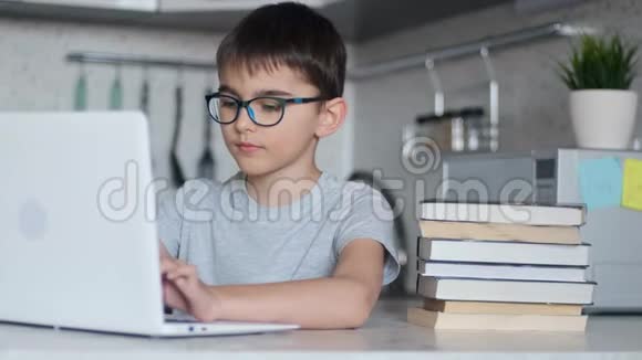 肖像一个孩子在家里坐在厨房的桌子旁看着相机用笔记本电脑做作业视频的预览图
