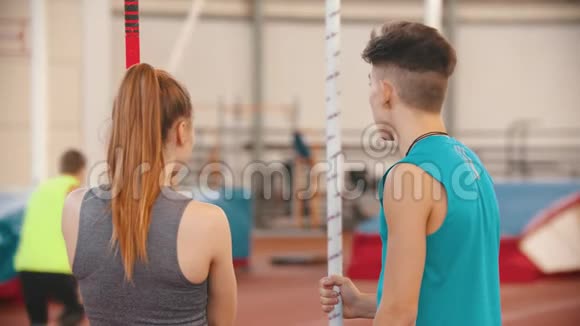 撑杆跳训练站在体育场上看其他运动员的男女青年视频的预览图