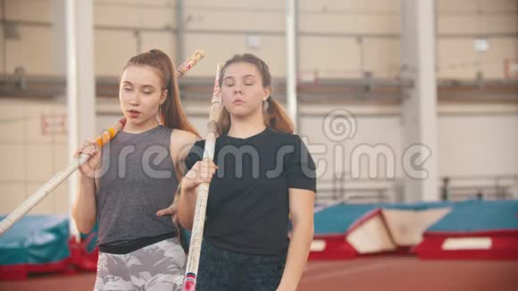 撑杆跳训练两个年轻的运动妇女站在体育场上举着杆子看着镜头视频的预览图
