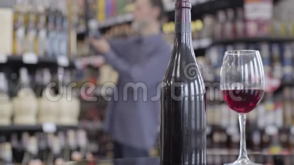 酒瓶和酒杯的特写镜头饮料站在前台模糊的白种人选择饮料视频的预览图