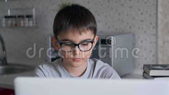 肖像小学生在餐桌旁的厨房里坐着用笔记本电脑做作业视频的预览图
