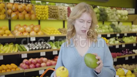 一幅严肃的高加索女人在杂货店选择水果作为她的女朋友带着多汁的橘子来的肖像视频的预览图