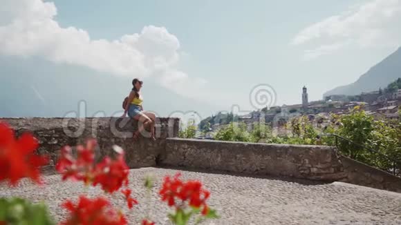 戴墨镜的年轻女子坐在石阶上欣赏小镇景色阳光明媚视频的预览图