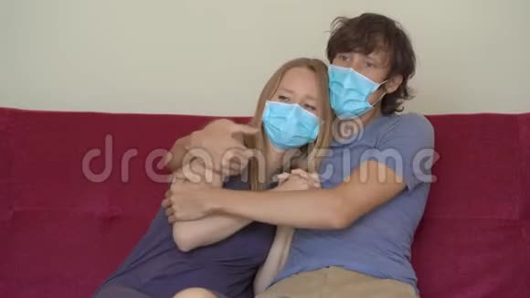一个年轻的男人和女人在自我隔离期间坐在家里的沙发上那个男人拥抱他害怕的妻子他们戴着医疗面具视频的预览图
