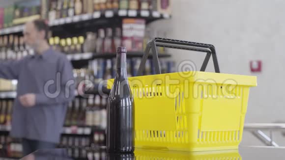 成年白种人来到酒铺的柜台把一瓶红酒放进黄色的购物篮里视频的预览图