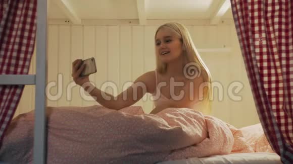 在宿舍房间里一位年轻漂亮的女士坐在床上用智能手机进行视频聊天视频的预览图