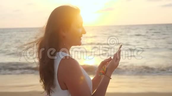微笑女孩在热带度假胜地海滩上使用智能手机视频的预览图