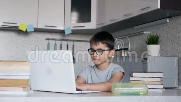 一个戴眼镜的小学生在家里坐在餐桌旁的厨房里用课本和一个视频的预览图