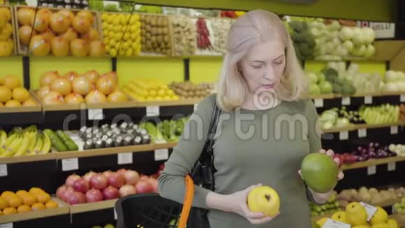 资深自信的高加索女人在杂货店里选择柚子和梨并决定两者兼而有之的肖像视频的预览图