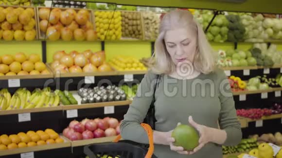 快乐自信的高加索女人在杂货店买水果的肖像年长的金发主妇把柚子放进篮子里视频的预览图