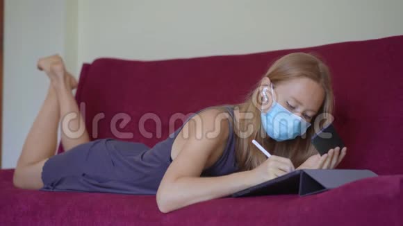 一位戴着医用面罩的年轻女子在冠状病毒自我隔离期间在家工作在视频的预览图