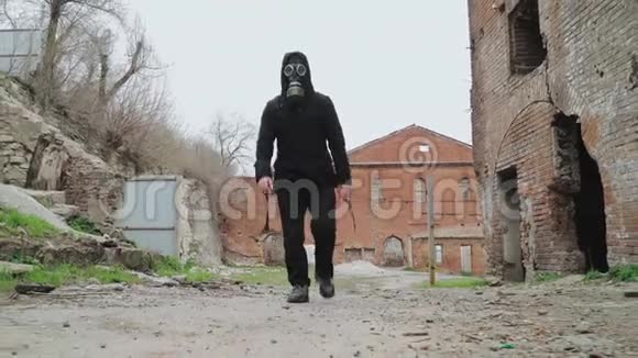戴着防毒面具和黑色衣服的男人背着一个背包在前城的废墟中行走视频的预览图