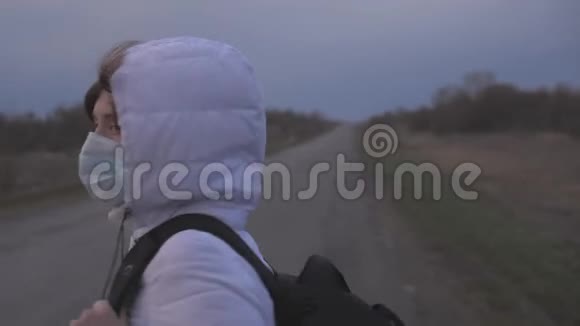 免费的女孩旅行者带着一个背包戴着保护性的医疗面具和引擎盖正步行出城在路上保护视频的预览图