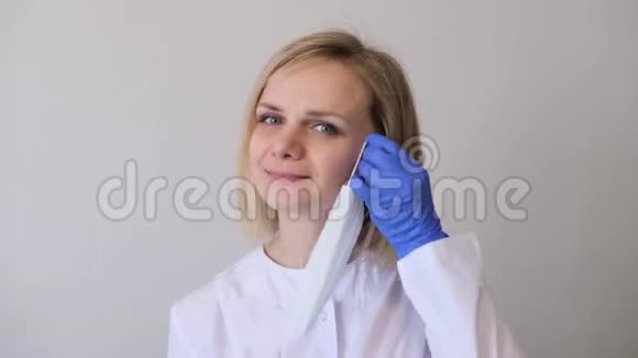 穿着白色制服和蓝色手套的金发女医生戴上医疗面具卫生治疗的概念视频的预览图