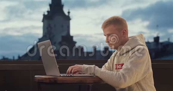 一个年轻人坐在屋顶上拿着笔记本电脑背景是一座古老的城市塔楼视频的预览图