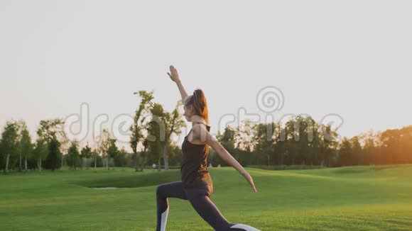 日落时分一个年轻的女孩站在绿草上做瑜伽视频的预览图
