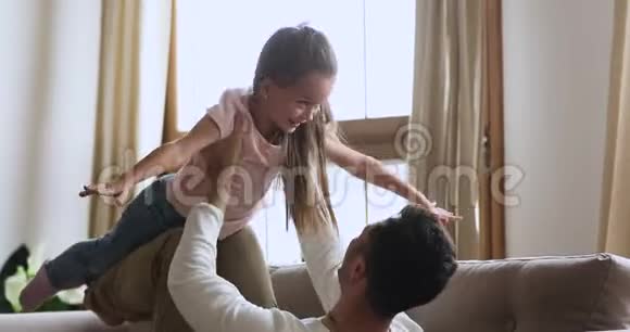 年轻的父亲躺在沙发上举起笑着的女儿视频的预览图