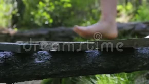 一个光着脚的女孩走在绿色森林里的木桥上腿部特写视频的预览图