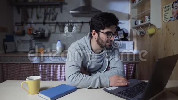 快乐的年轻商人晚上在家厨房里做笔记本电脑视频的预览图