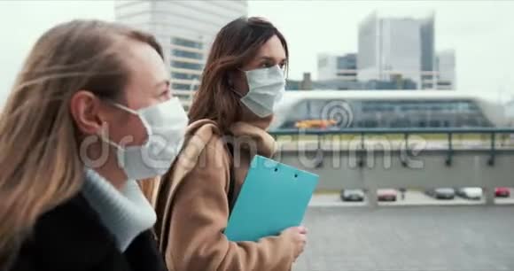 侧视两名年轻的高加索医生妇女戴着口罩走在空荡荡的城市街道上锁着剪贴板视频的预览图