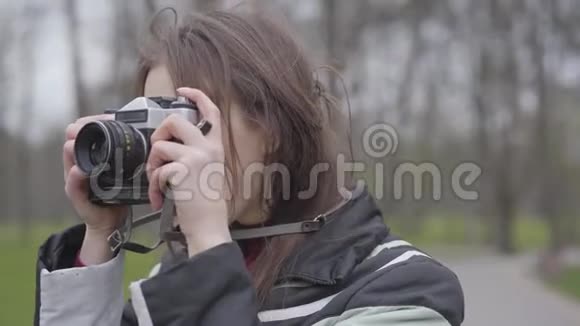 用相机拍摄正面女性摄影师的特写肖像年轻兴奋的女人在公园里拍大自然的照片视频的预览图