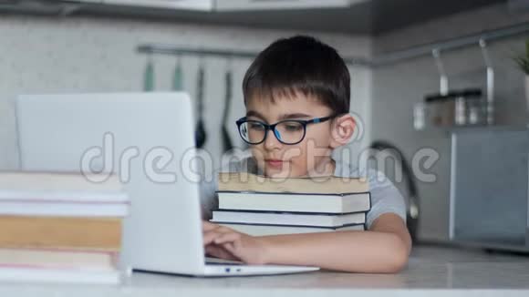 一个小学生在餐桌旁坐在厨房里做家庭作业使用大量的教科书和笔记本电脑网上在线视频的预览图