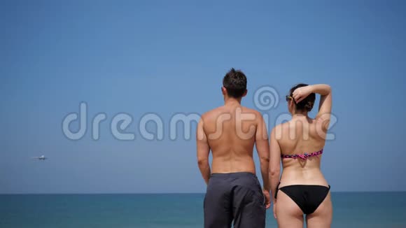 男人和女人站在海洋附近看着接近的飞机视频的预览图