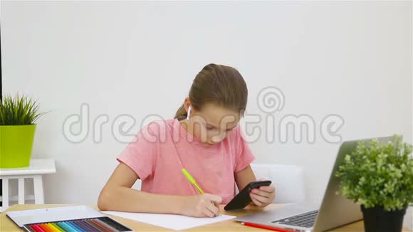 严肃的女学生坐在桌旁拿着笔记本电脑和课本做作业在家学习视频的预览图