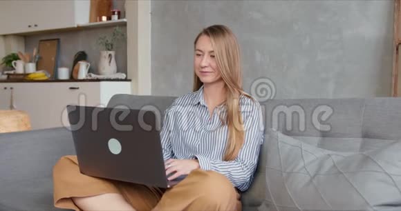 迷人的健康年轻白种人金发经理女士在家沙发上隔离期间使用笔记本电脑在线购物视频的预览图
