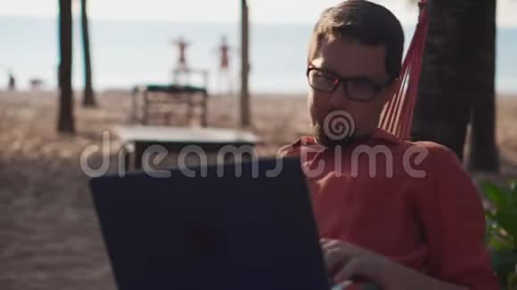 在沙滩吊床上用笔记本电脑放松视频的预览图