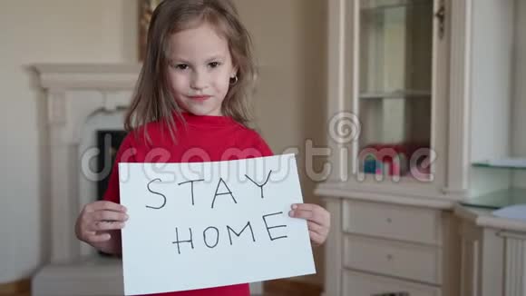 呆在家里的概念穿着红色N恤衫的小女孩举着牌子说呆在家里保护病毒照顾她视频的预览图