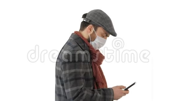 时尚男人在医疗面具行走和使用智能手机的白色背景视频的预览图