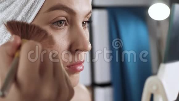 女孩把脸上的光泽放在皮肤上浴室里头上戴毛巾的漂亮女孩用荧光笔或古铜色笔视频的预览图