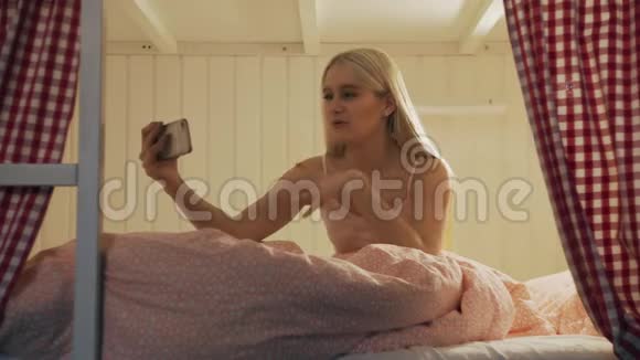 在宿舍房间里一位年轻漂亮的女士坐在床上用智能手机进行视频聊天视频的预览图